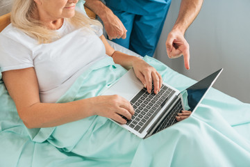 Naklejka premium cropped shot of senior woman using laptop with blank screen in hospital bed