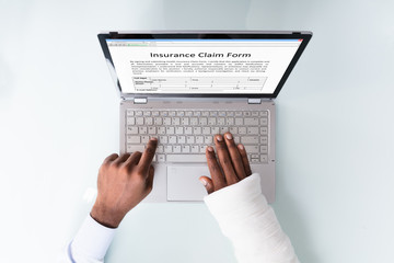 Businessman With Bandage Hand Filling Insurance Claim Form