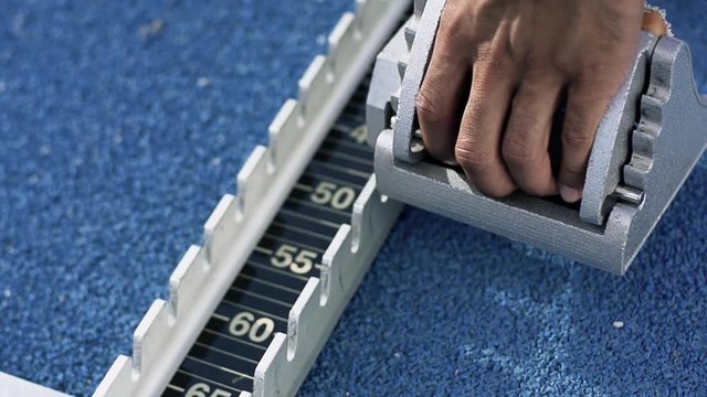 young man is preparing the start block on a blue running stadium
