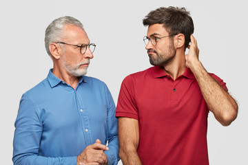 War of generations concept. Displeased bearded mature father and son look angrily at each other,...