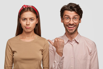 Displeased European female being abused after quarrel with boyfriend who indicates at her with positive expression, dressed casually, isolated over white background. Two best friends indoor.