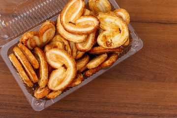 Palmier biscuits - french cookies made of puff pastry (also called palm leaves, elephant ears or french hearts) packed in plastic box on wooden table