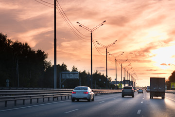 Cars on busy road driving in evening sunset. highway with metal safety rail or barrier