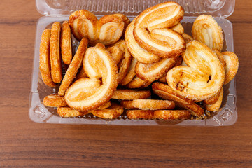 Palmier biscuits - french cookies made of puff pastry (also called palm leaves, elephant ears or french hearts) packed in plastic box on wooden table