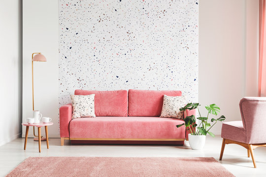 Real photo of a pink, velvet sofa, plant, coffee table with pot and cups on a lastrico wall in a living room interior