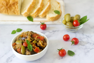 Caponata or ratatouille from a variety of vegetables served with ciabatta and olive.