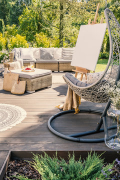 Hanging chair on wooden patio with easel and rattan table in front of sofa in the garden