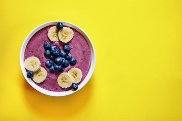 Smoothing bowl with blueberries and banana on a yellow background, vegan, organic, flatlay, copyspase