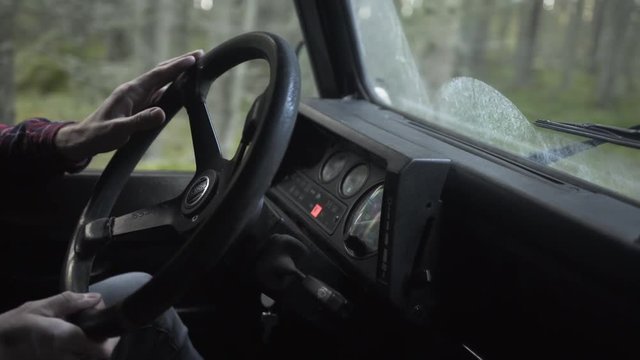 Outdoorsy man with a beard by the wheel driving a vintage 4x4 in forest, handheld