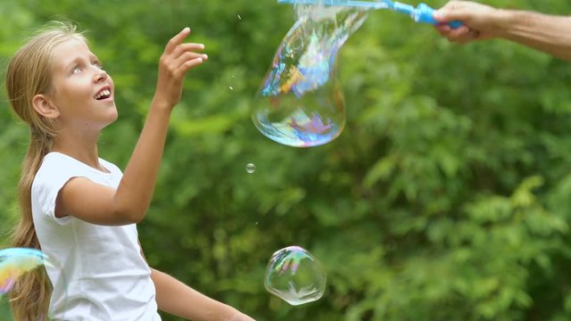 The nine-year-old girl plays with soap bubbles in the summer garden. Slow motion. 
