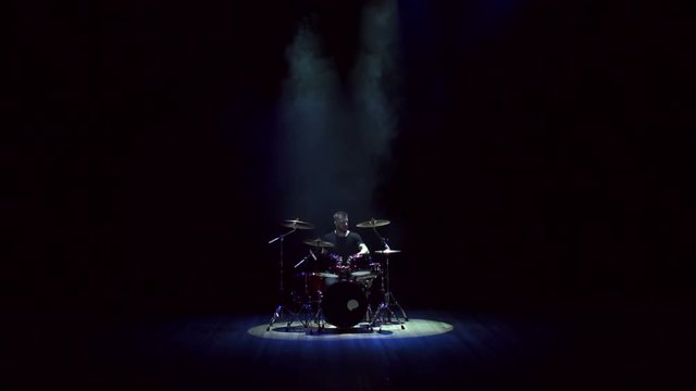 Man plays musical percussion instrument with sticks on a black background, a musical concept with the working drum, beautiful lighting on the stage.