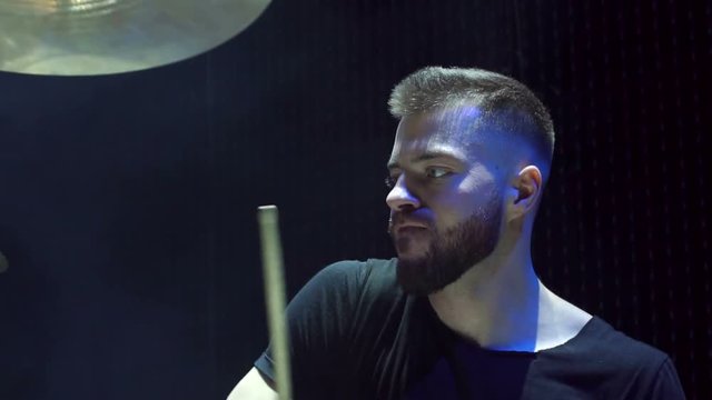 Close-up face of emotional bearded male drummer playing drums on a black background.