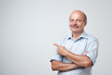 Senior man in blue shirt pointing with index finger to important information on copyspace