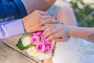 Couples hands wearing their wedding rings resting on the wedding bouqet