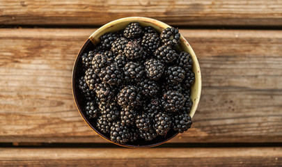 Closeup of a bowl full of fresh ripe blackberries on wooden background. Concept - healthy food.
