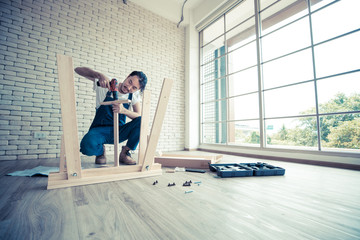 Young man working as handyman, assembling wood table with equipments, concept for home diy and self service.in the office there is white brick block.