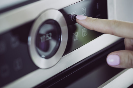 Female finger is touching the button of modern panel of electric oven.