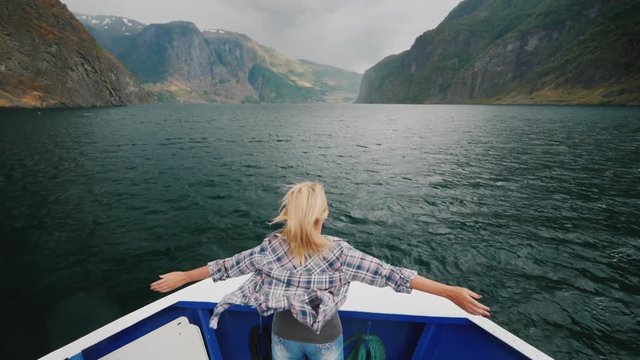 A woman is standing on the bow of the ship sailing over the fjord in Norway. Enjoys the journey, the wind waves her hair