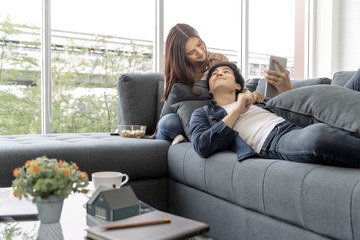 Asian teenage couple make eye contact relaxing on  sofa  by the window relax in the luxurious room.