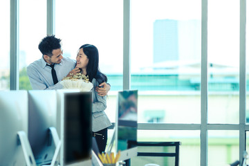 Asian businessman and businesswoman is a flirting in modern office with flowers in hand, concept for love in business.
