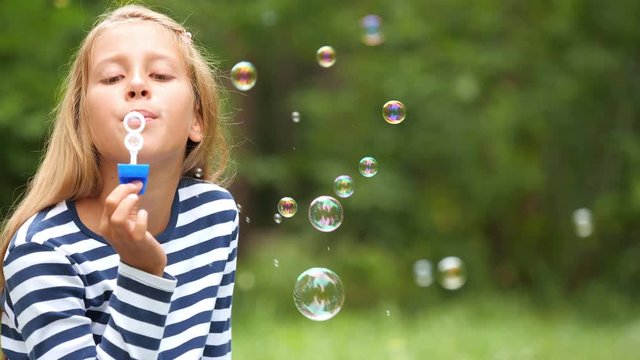 The nine-year-old girl plays with soap bubbles in the summer garden.
