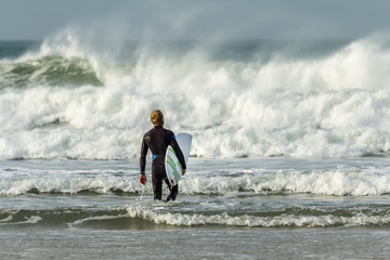 Young Man entering waves with surfboard