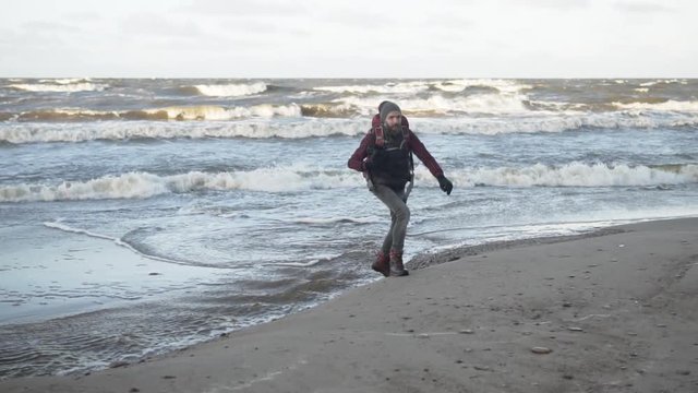 Outdoorsy photographer with a backpack walking by a stormy sea, slow motion, gimbal tracking shot