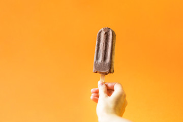 Girl's hand holding chocolate ice cream on a bright orange background.