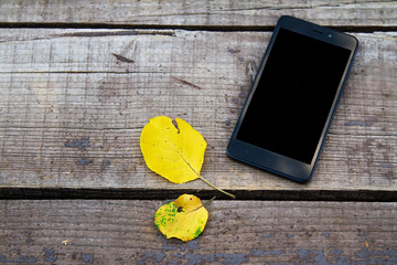 mobile phone on a wooden old autumn background, near the yellow autumn leaves.