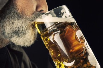A bearded friar (Franciscan religious man) eagerly drinking cold beer from a giant mug.
