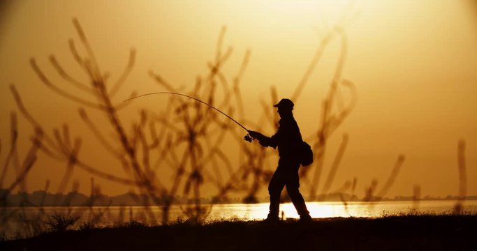 A proficient fishman catching fish with professional spinning rod in hands from the shore. lake in golden sunset 4k