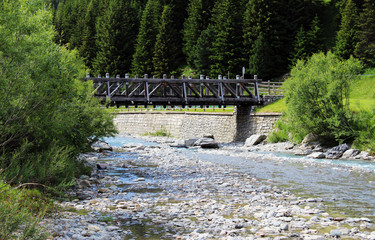 Side view of a wooden pedestrian bridge crossing a mountain creek