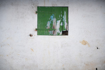 Altes Fenster mit grünem geschlossenem Fensterladen in einer weißen Wand.