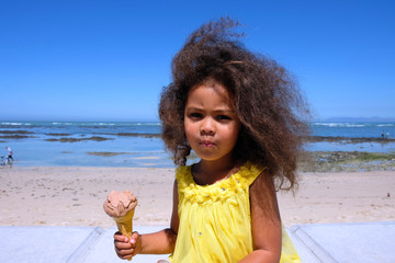 Girl in a yellow dress on the beach eating ice cream