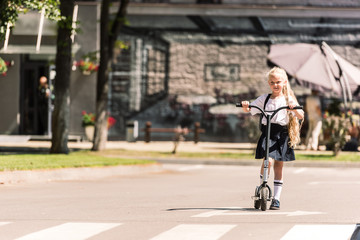 beautiful little schoolgirl with long curly hair riding scooter at sunny day