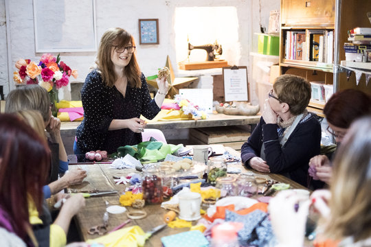 Group of women sitting around a table in a workshop, making fabric flowers.