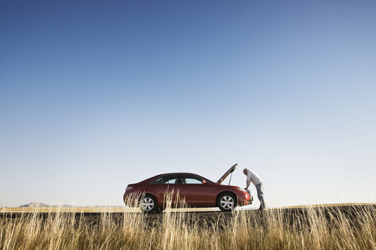 A man looking into the engine compartment of his car parked along a highway in eastern Washington State, USA.