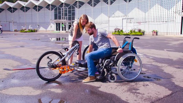 Happy young disable man is changing wheelchair for hand bike. His wife is helping him