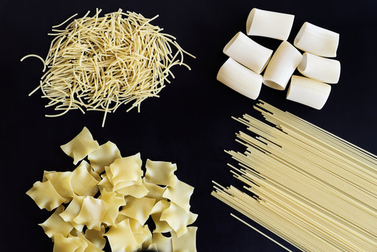 Four different types of pasta are laid out on black background