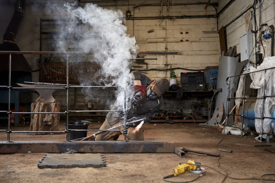 Artisan metalworker at work in a workshop working, soldering a metal fence. 