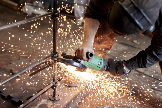 An artisan metalworker at work holding an angle grinder, workng on a metal fence. 