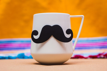 Paper black mustache decoration on white cup against blurred background