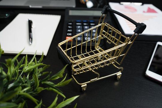 Gold cart, cash and gadgets on a black table.