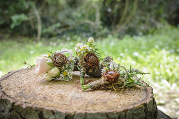 weeding boutonnieres with rose and pine cone on a wooden stump.