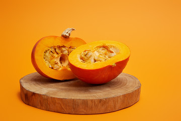 close-up view of ripe sliced pumpkin on round wooden board on orange background