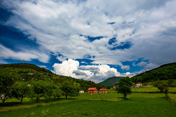 Fototapeta na wymiar Serbian rural village green springtime landscape, mountains in Serbia are very beautiful, near Valjevo. Valley and hills. White and red houses, farmland and spring forest. Great European countryside
