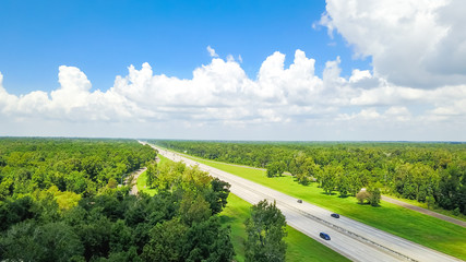 Aerial horizontal view of Interstate 10 highway near rest area with exit and service road. Scenic road surrounded by green oak trees under cloud blue sky in USA. Industry and transportation background