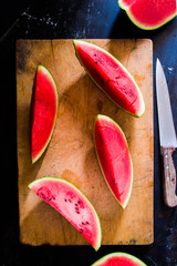 Watermelon cut  on a wooden cutter over a black bord,   top view, low key natural light.