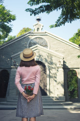 Woman holding flower in hand and standing in front of church.