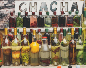 traditional georgian alcohol drink chacha in bottles with different fruits and herbs selling at market